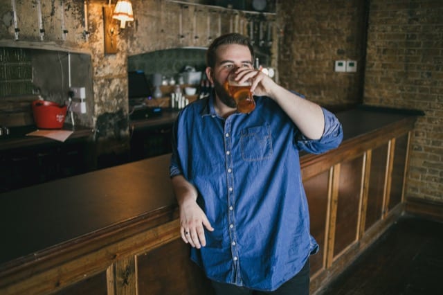 Man in blue jean shirt at a bar drinking a pint of beer for his Perfocal lifestyle photoshoot