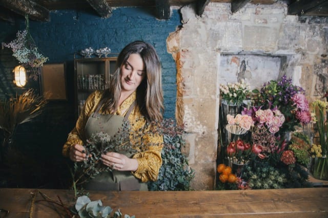 Woman in yellow dress begins making a bouquet of flowers for the florist's lifestyle photoshoot