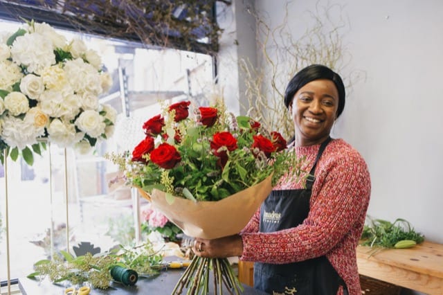 Black woman creates bouquet of red roses at her florist's lifestyle photoshoot