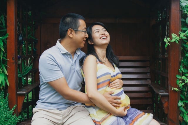 asian couple both cradle the wife's pregnant belly whilst being photographed