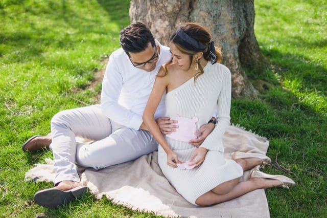 pregnancy announcement photo with a couple in white holding baby clothes