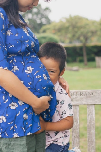 young child smiles at the camera and hugs his mother's baby bump