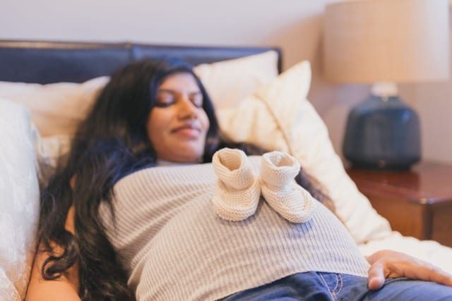 pregnant woman lovingly glancing at her belly and the two knitted boots resting on top of it