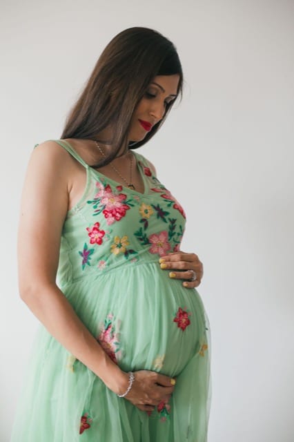woman in floral dress having her photo taken whilst holding her large baby bump