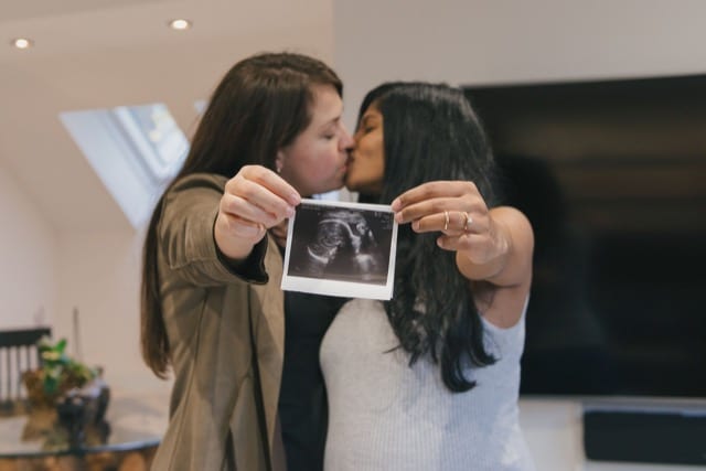two women kissing and celebrating their pregnancy by holding a CT scan photo