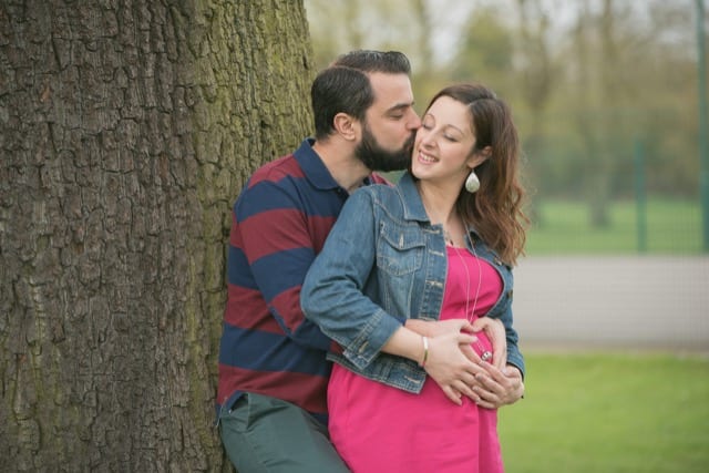 couple resting on a tree as husband kisses pregnant wife