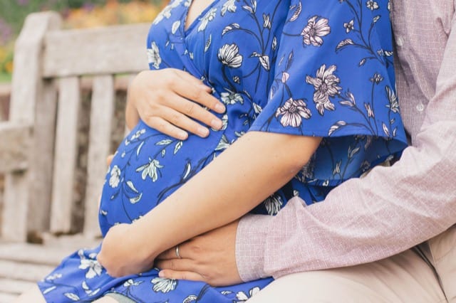 couple on a bench in london park cradling her baby bump
