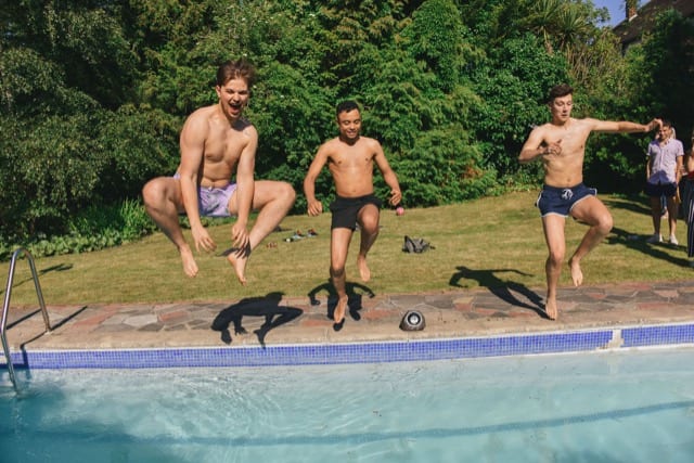 three men jumping into the pool on a house party