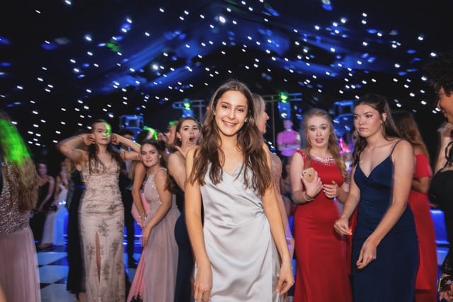 a young girl poses at her prom on the dimly lit dance floor