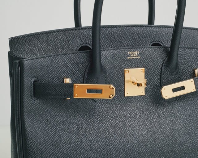 a close up of a black leather hermes bag with gold detailing