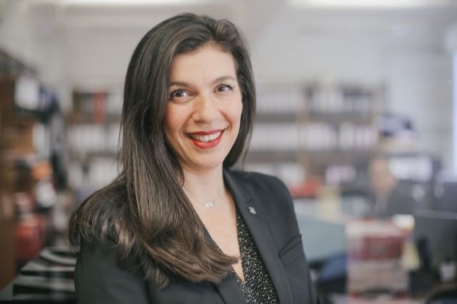 Close up of a woman in a black suit posing for her headshot in front of a library