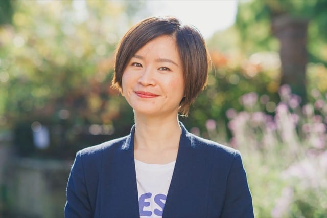 asian woman in a blazer smiles for her perfocal headhsot in her office's garden