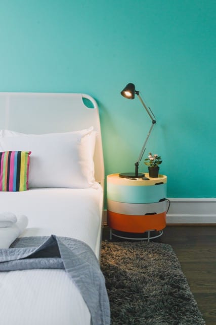 A close up of a double bed and its nightstand, with an industrial style lamp and mint blue wall