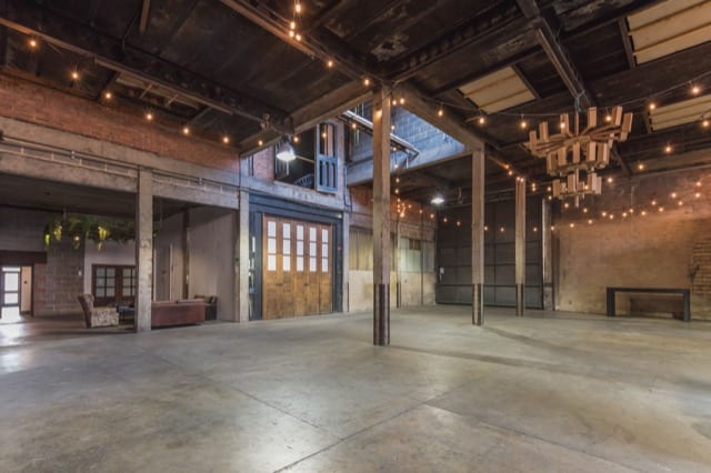 An expansive open warehouse space with concrete floors, brick walls and hanging fairy light