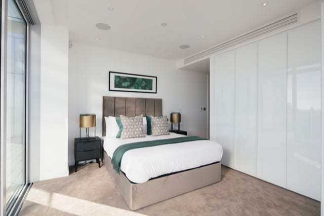 A double bed with grey pillows and throw in a bright modern room, overlooking a large window