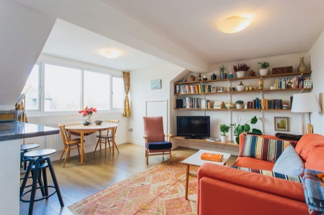 The living room of a bright and airy modern apartment, with lots of books and plants