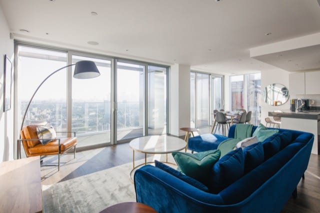 A blue suede sofa in a high rise studio appartment overlooking the London Skyline
