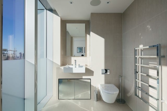 A well lit bathroom with large grey tiles and a modern design