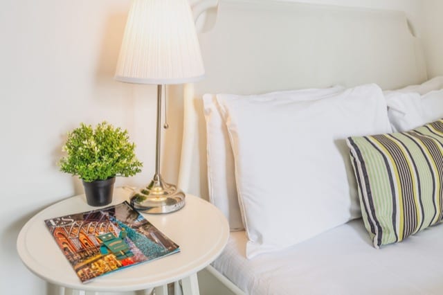 Close up shot a small double bed and the nightstand with a lamp, thyme plant and magazines