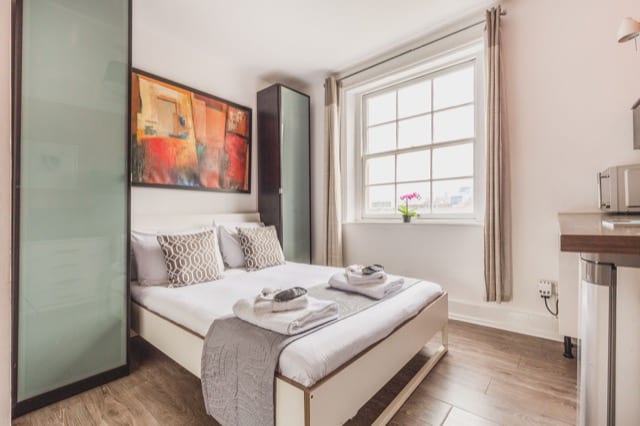 A double bed nested between two tall cupboards dressed with a grey bed throw and white towels