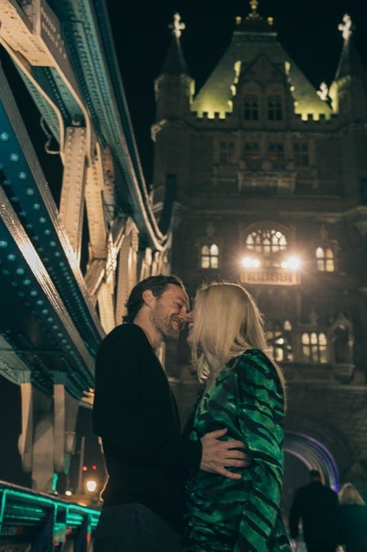 Smiling couple embrace on Tower Bridge at night