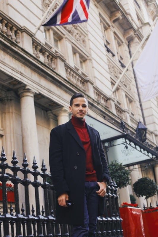 Smartly dressed man smiles at camera in front of London hotel