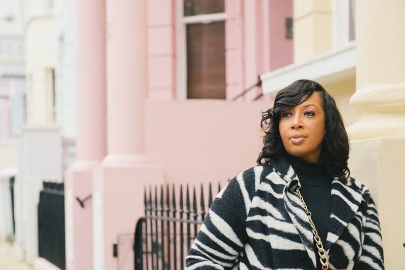 Woman in zebra print coat poses in front of colourful houses in Notting Hill, London