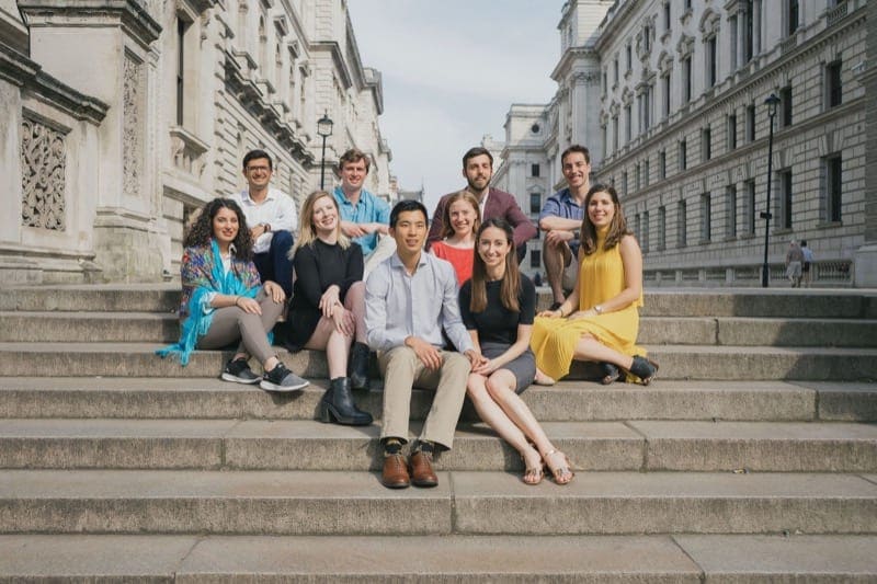 Group of student friends sit together on London steps in the summer time