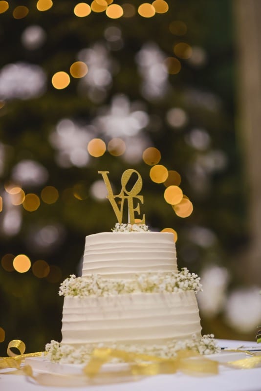 Ivory white wedding cake with sweet icing, decorated with white flowers and a cake topper that spells love.