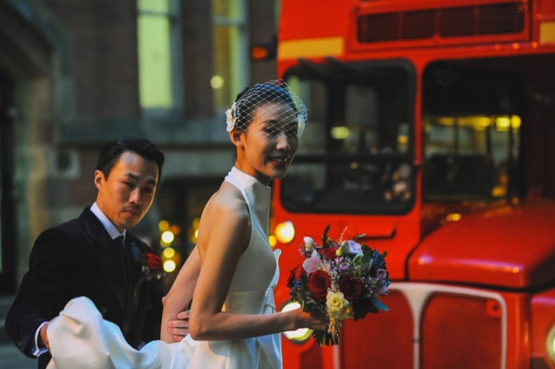 Chinese couple have manchester wedding shoot in front of bus in white gown and veil with groom carrying dress tain