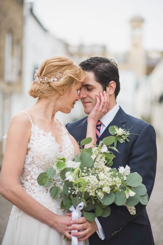 Blonde woman cupping husband's face in kensington mews dressed in white wedding gown with a eucalyptus bouquet.
