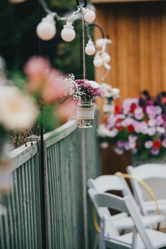 Small bouquet of dried flowers in a glass jar hanging from the garden fence at a garden wedding photoshoot