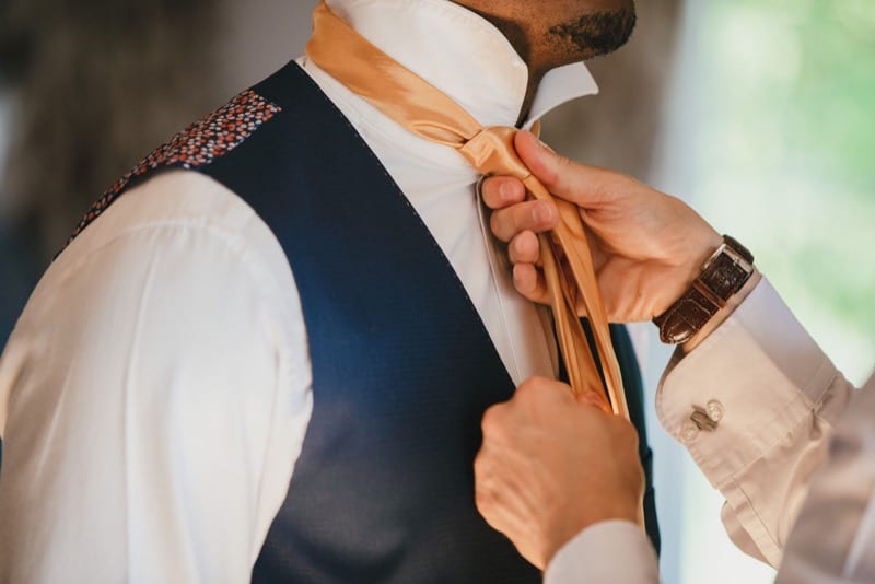Pre-wedding preperations. Groom has his gold tie tied by his best man